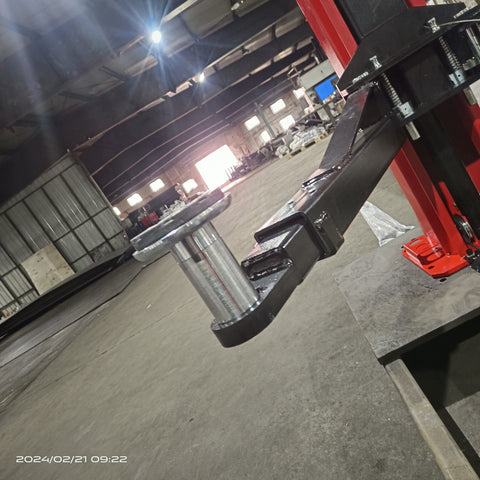 2-post vehicle lift in red installed in garage
Close-up of lifting arms and safety lock mechanism
Base of hoist with truck tires for scale
Top bar and hydraulic system – JH5000F model