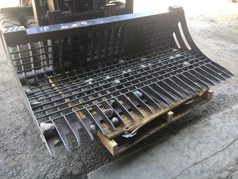 96" skid steer rock bucket with ½" spacing
Heavy-duty skeleton rock bucket on gravel
Close-up of angled bar structure
72" deluxe rock grapple for small rocks and debris
Skid steer lifting rock bucket attachment