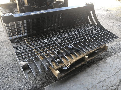 96" skid steer rock bucket with ½" spacing

Heavy-duty skeleton rock bucket on gravel

Close-up of angled bar structure

72" deluxe rock grapple for small rocks and debris

Skid steer lifting rock bucket attachment

