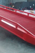 Forklift-compatible heavy-duty portable dock ramp on pavement. Hydraulic lift steel ramp for loading docks and truck beds. Close-up of industrial safety railings on mobile dock platform