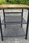 Rustic end tables in a cozy living room setting with sofa and lamp

Side View: Square wood top table with black mesh shelf

Angled View: Rustic wood and black metal table with adjustable shelf

Front View: Front profile of industrial end table with wood top and mesh shelf

Top View: Close-up of wood grain tabletop with rounded edges
