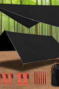 Camping tarp with aluminum stakes and wind ropes laid out
4-in-1 waterproof tarp in use as rain shelter in forest
Black tarp covering picnic area in outdoor campsite
Folded tarp in carry bag with accessories shown separately